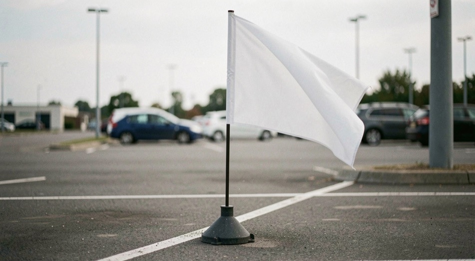 Drapeau publicitaire vierge planté dans un pied lesté sur un parking, toile prise par le vent